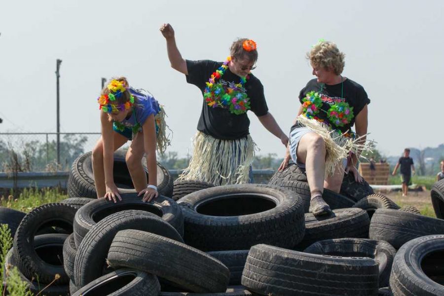 This family, dressed in luau attire complete with grass skirts, coconut bras, and vibrantly colored flower leis, climb over a pile of tires on their way to the finish line.