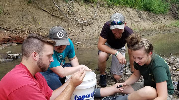 Daniel Akin (left) and Molly Takacs (right) teach Cody Hart (middle left) and Jack Neske (middle right) how to tag orangethroat darters for Takacs’ study. Akin is using funding from the Undergraduate Scholars Grant to work on a different project on minnows. (Courtesy photo by Emmy Dunlap)