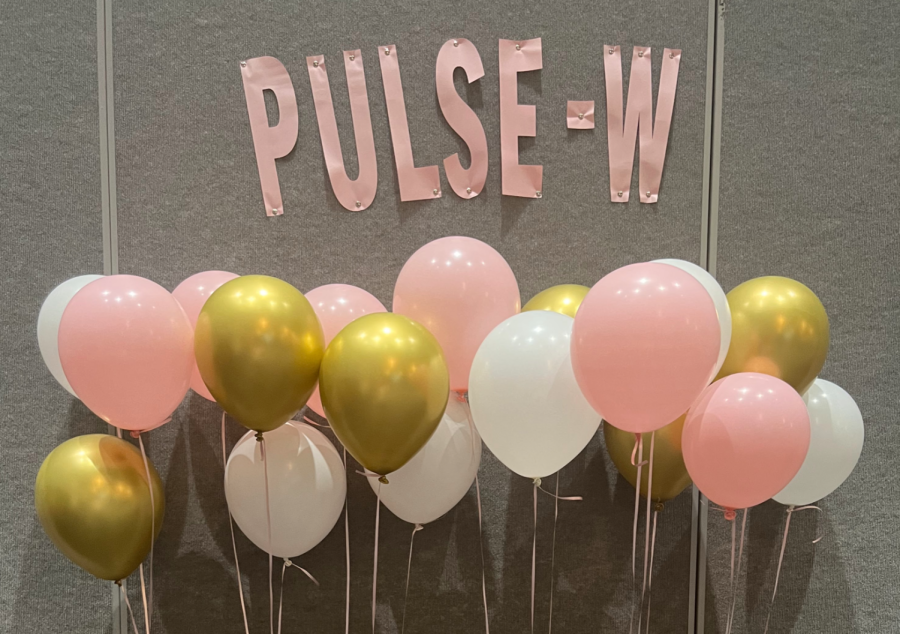 Pulse - W has pink, white and gold balloons set up in front of dark gray wall.