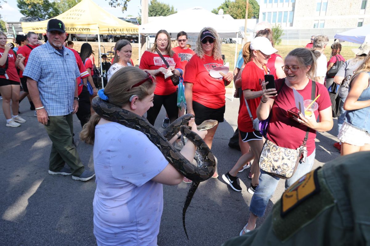 An attendee of Warrensburg's annual street fair, Get the Red Out, holds a snake at a booth for exotic animals while her photo is taken on Sept. 11. Get the Red Out hosted 171 vendors and was held before the University of Central Missouri’s first home football game of the season.